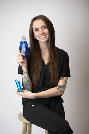 Person in black clothing poses with blue bottle against white background in three similar studio shots.