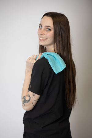 Person wearing black sweater with turquoise fabric detail on shoulder poses against neutral background.