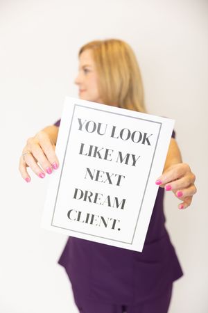 Person in purple holding sign that reads 'You look like my next dream client' against white background.