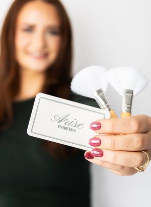 A hand with red nail polish holds a business card against a blurred background.