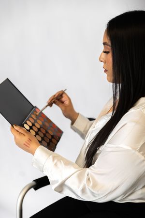 A person with long dark hair in a white shirt holds and reads from a book against a white background.
