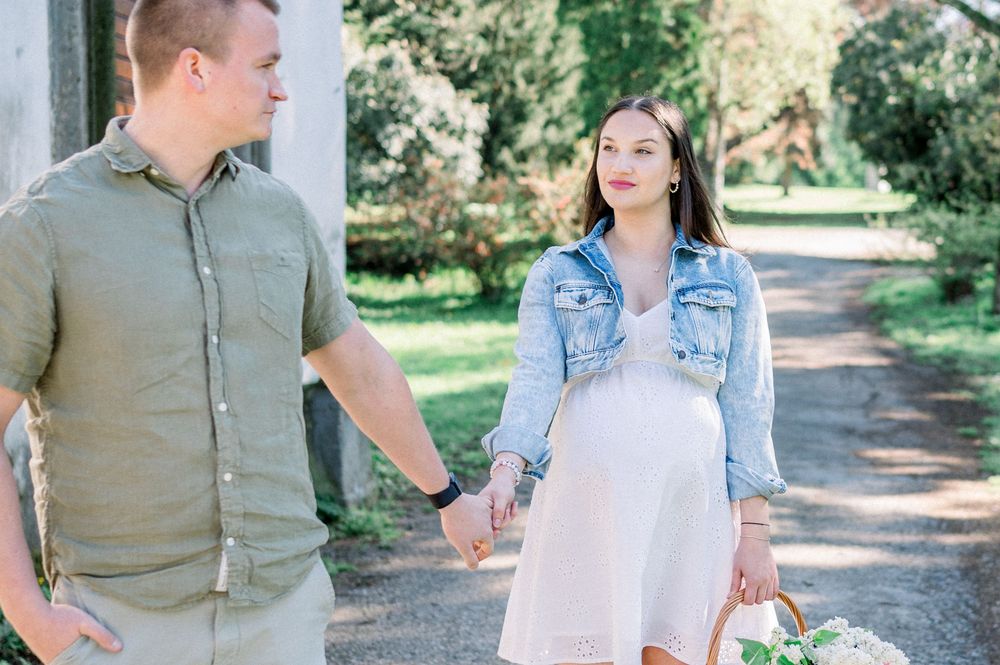 A couple walks hand in hand along a tree-lined path during a spring photoshoot.