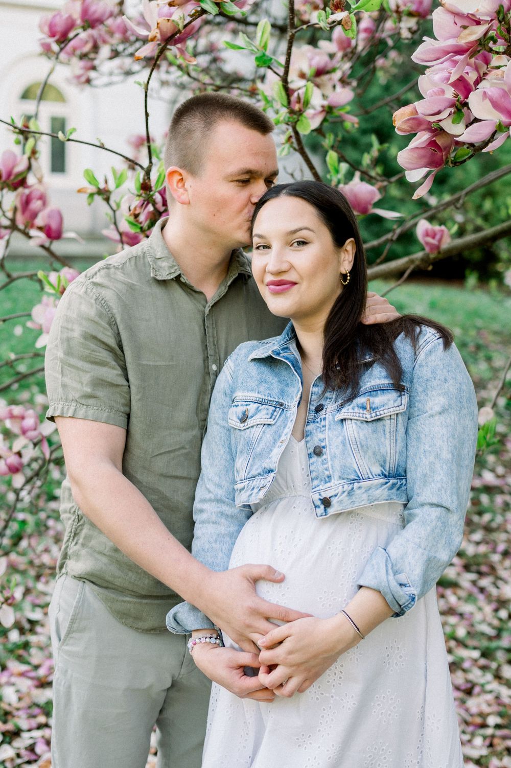 A couple embraces under blooming pink magnolia trees in a romantic spring photoshoot.