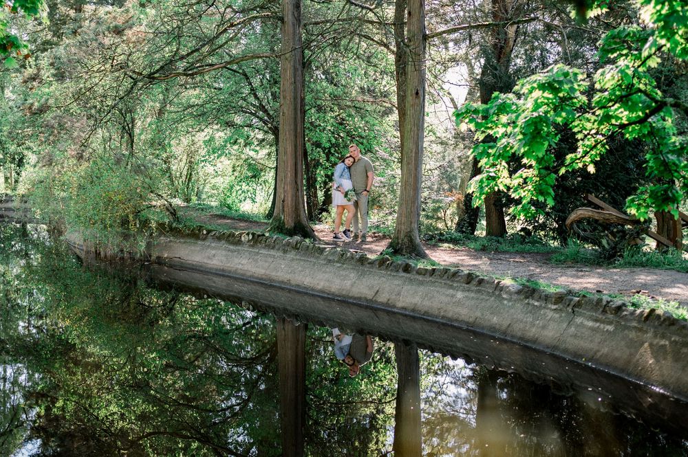 Rustic wooden bridge spans across a serene pond in a lush green park setting.