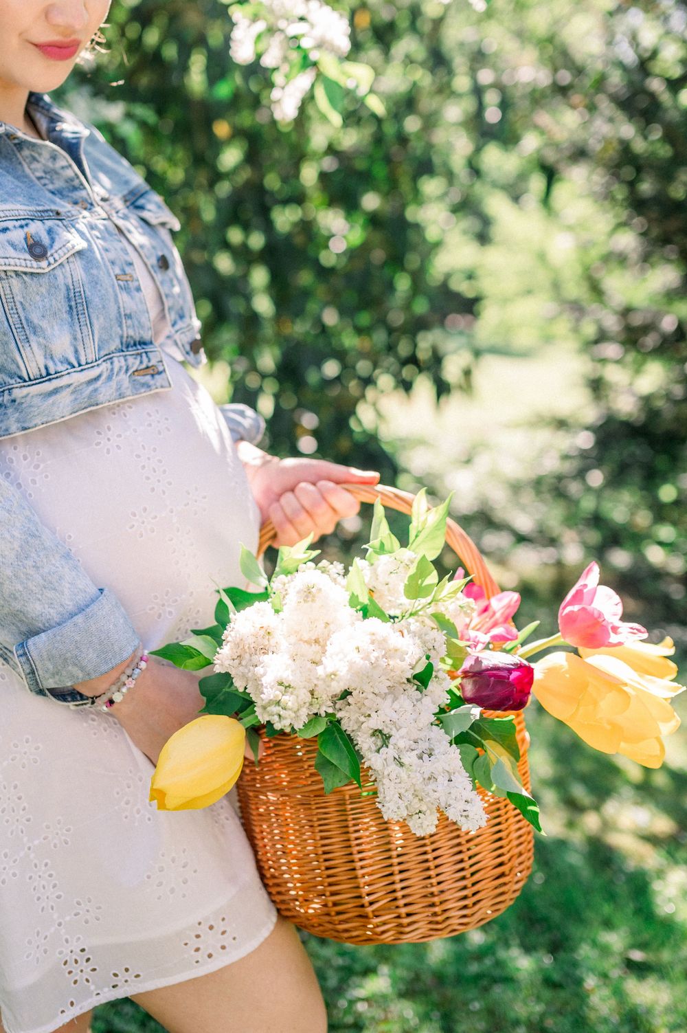 A wicker basket filled with colorful tulips and white lilac flowers against a green garden background.