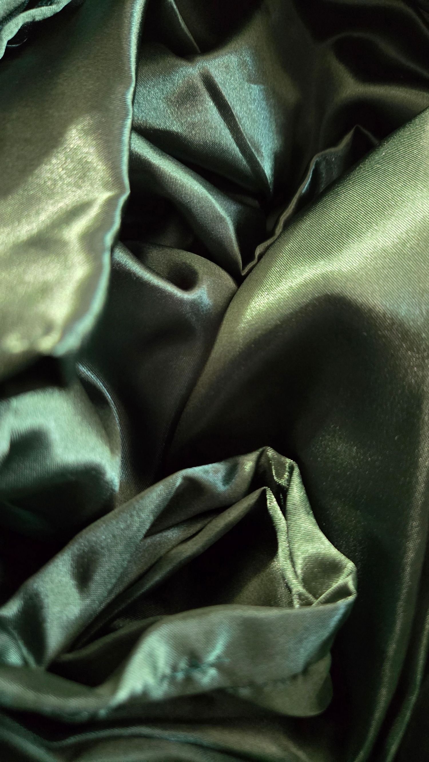 Dark green satin fabric with elegant folds and creases creating a luxurious textured background.