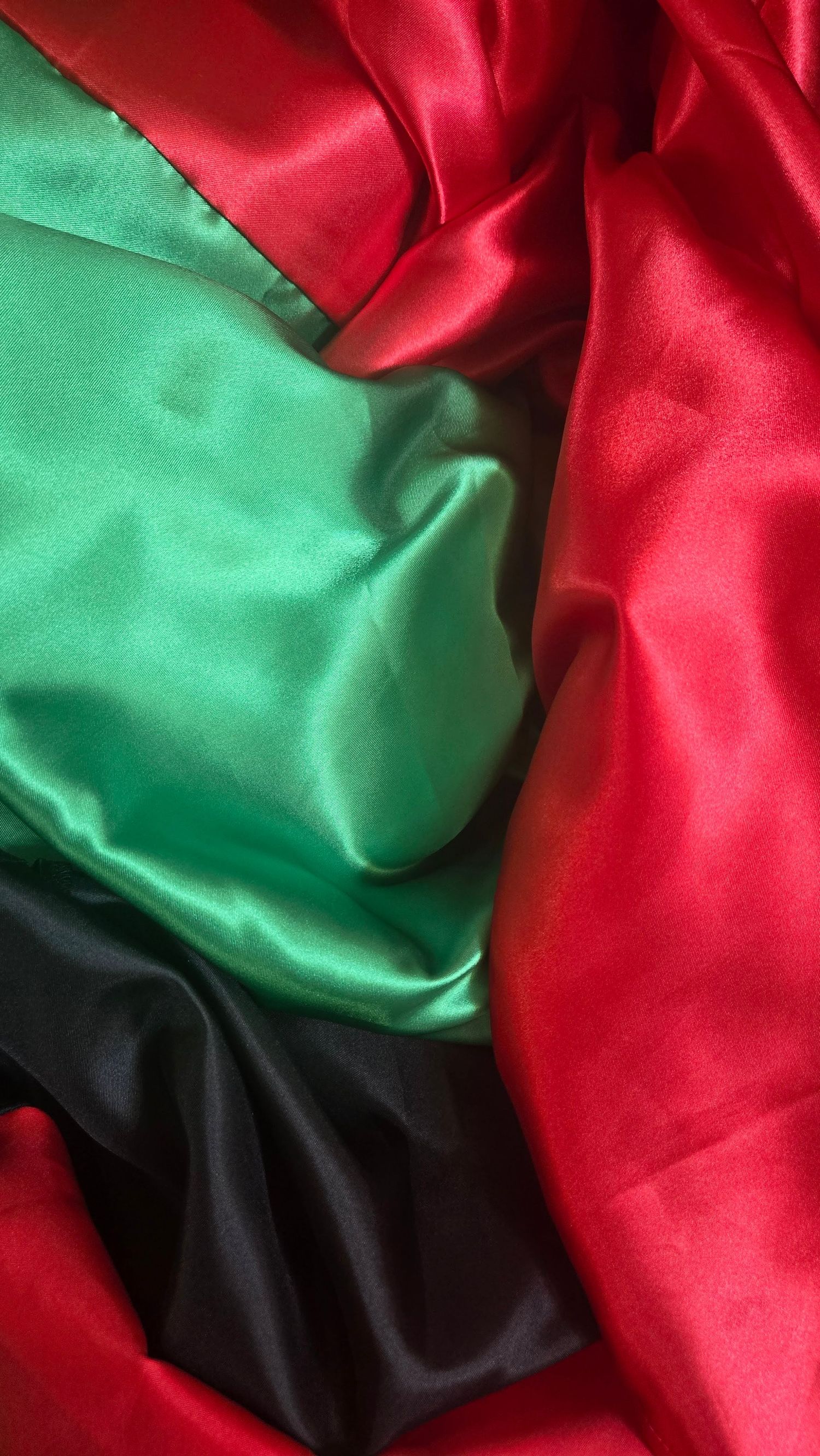 Silky fabric in red, green and black colors rippling together in a wave-like pattern.
