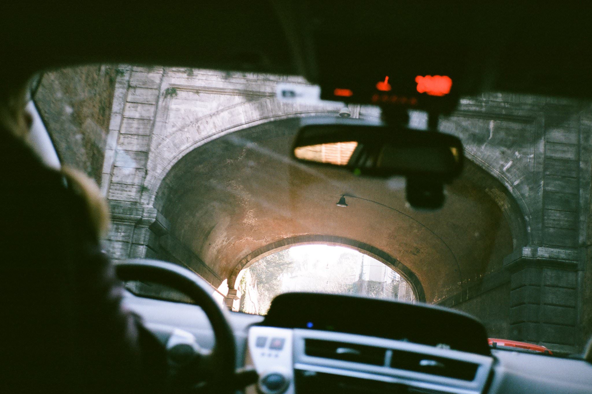 A dark security camera footage shows a car driving through what appears to be a parking garage or tunnel structure.