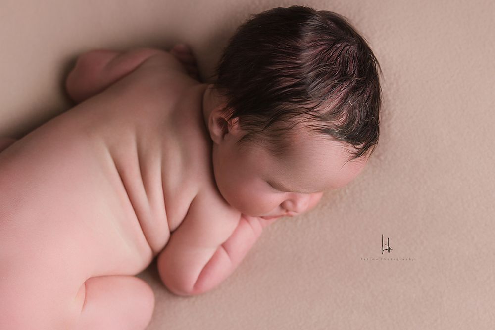 A sleeping newborn baby in soft pink tones lies peacefully on a cozy blanket during a professional photo session.