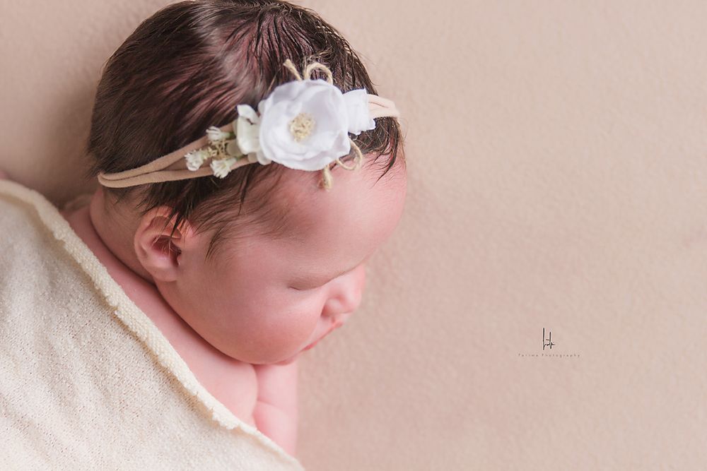 Newborn photography session featuring soft pink tones and delicate white floral headband.