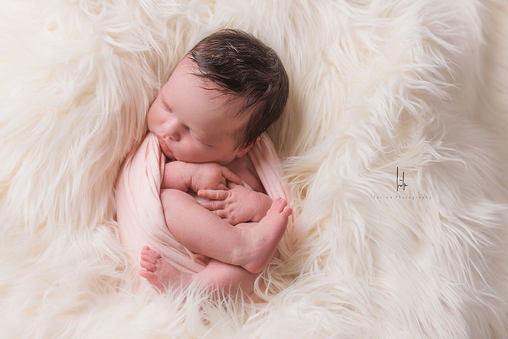 Peaceful sleeping newborn posed on fluffy white fur blanket in gentle natural light.