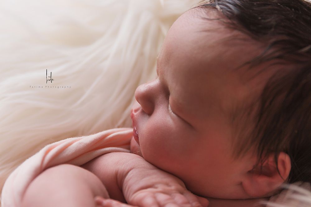 Sleeping newborn baby in soft pink light rests peacefully on white blanket.