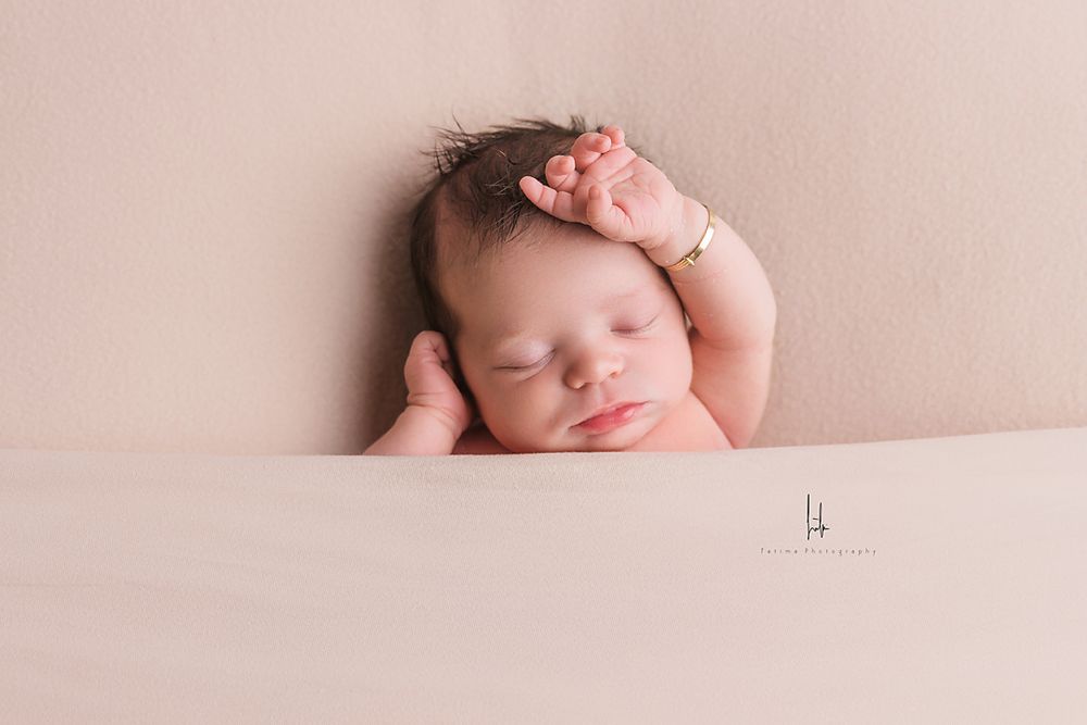 A sleeping newborn baby wrapped in soft pink fabric lies peacefully during a professional photo session.