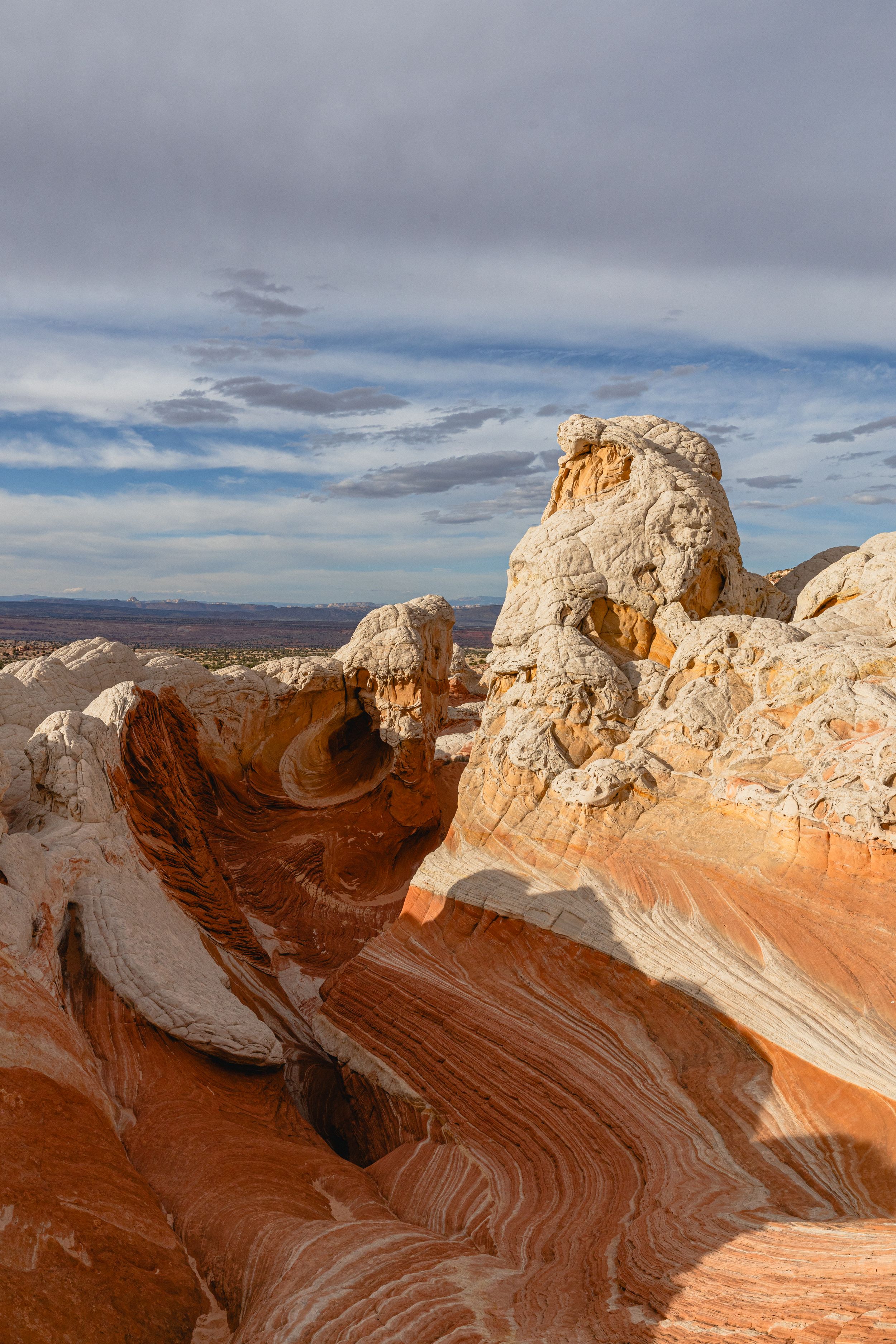 Panoramic view of White Pocket's swirling sandstone formations in Arizona against a cloudy desert sky.