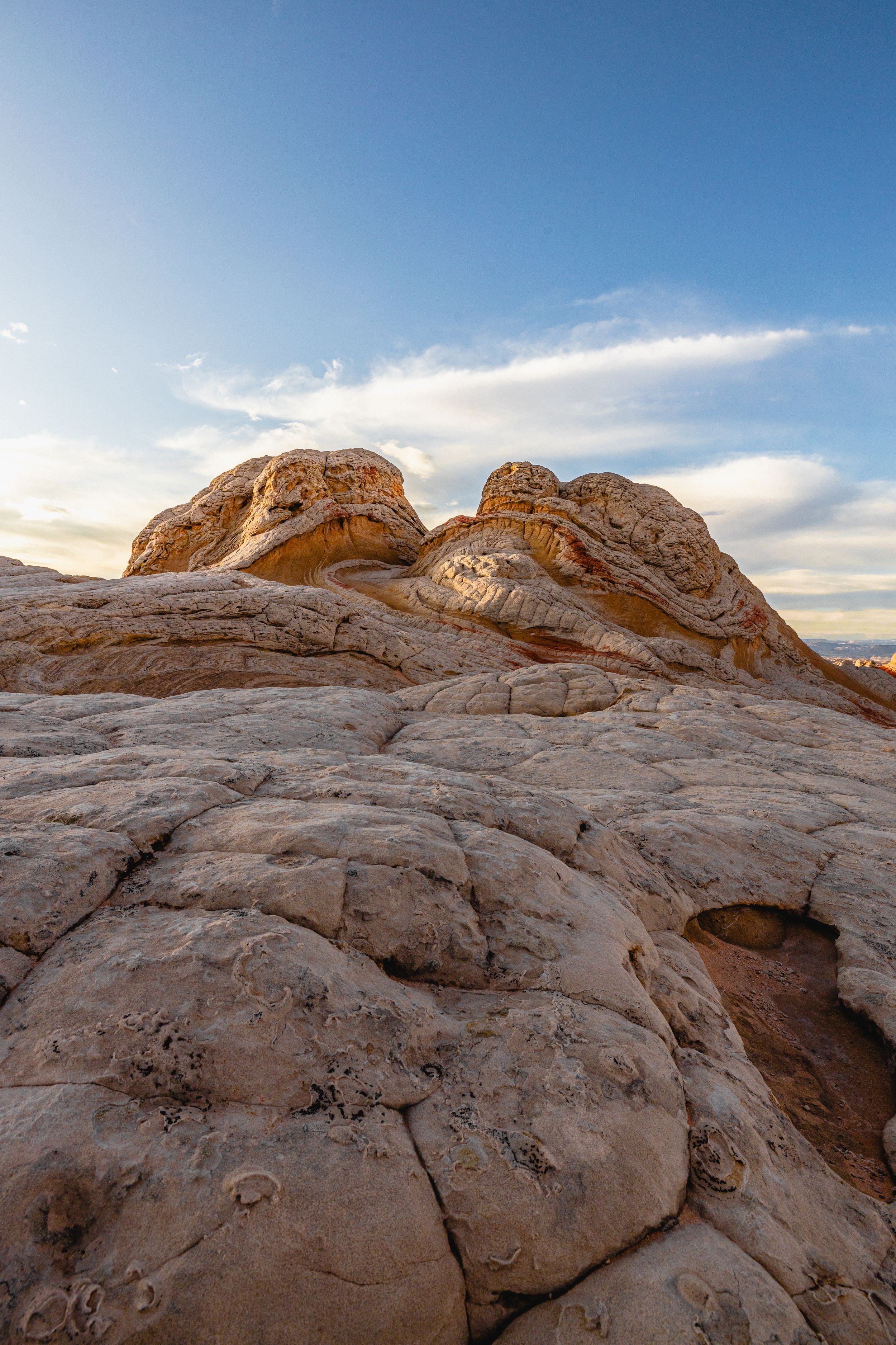 Rugged sandstone formations rise against a blue sky with wispy clouds in White Pocket, Arizona.