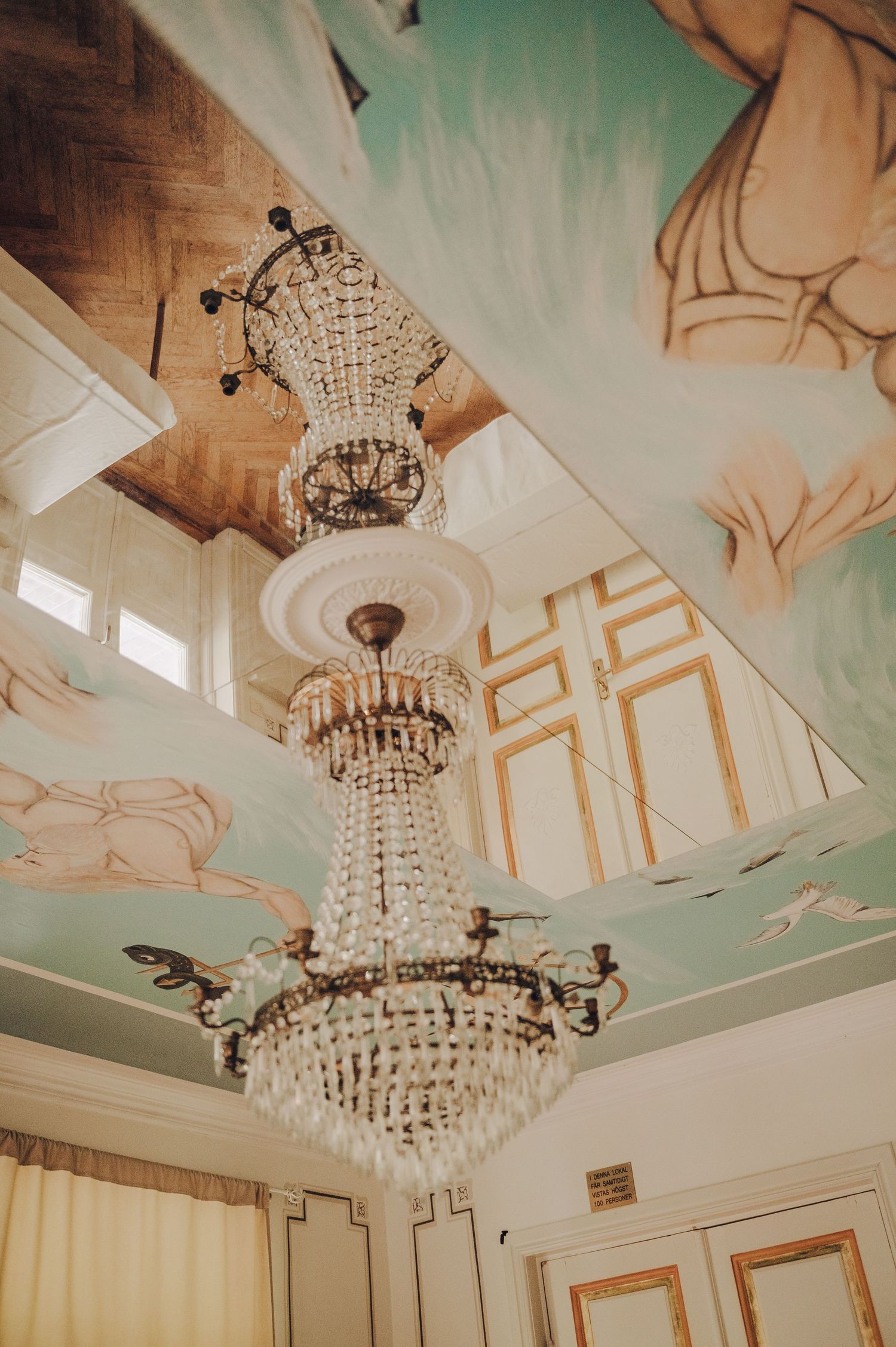Crystal chandelier hangs from mint green ceiling with ornate gold trim details in an elegant room interior.