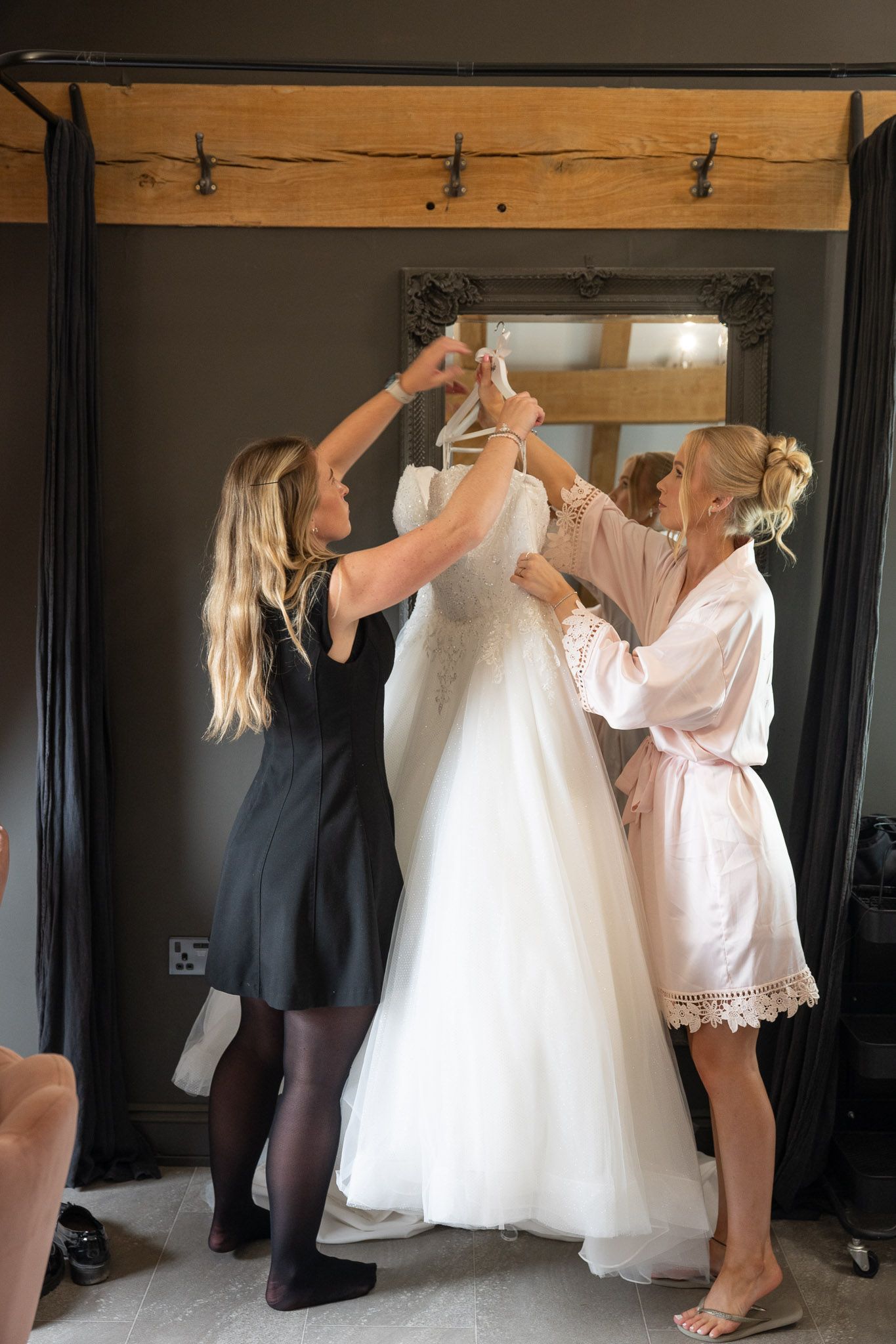 Bridesmaids and staff are hanging the brides dress up in the bridal room at The Old Kent Barn.