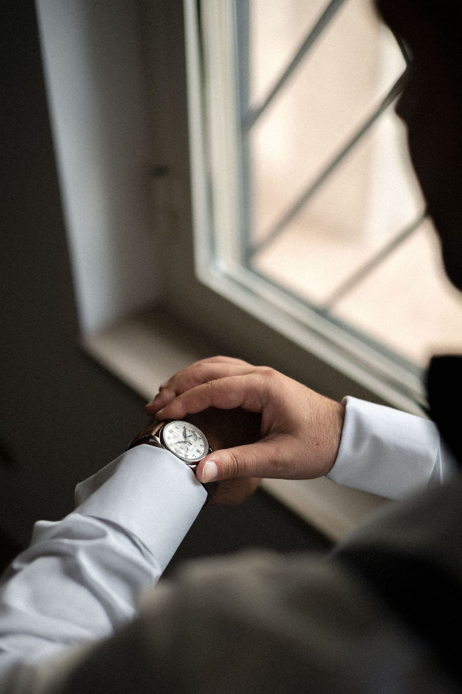 Close-up view of hands adjusting white dress shirt cuffs in soft window lighting.