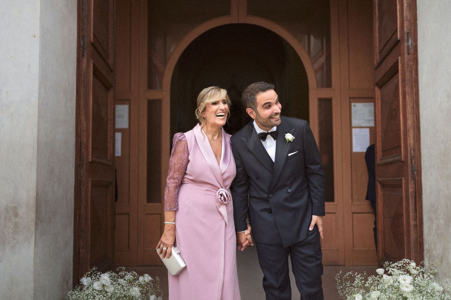 A bride and groom share a tender moment together while posing for photos in front of wooden doors.