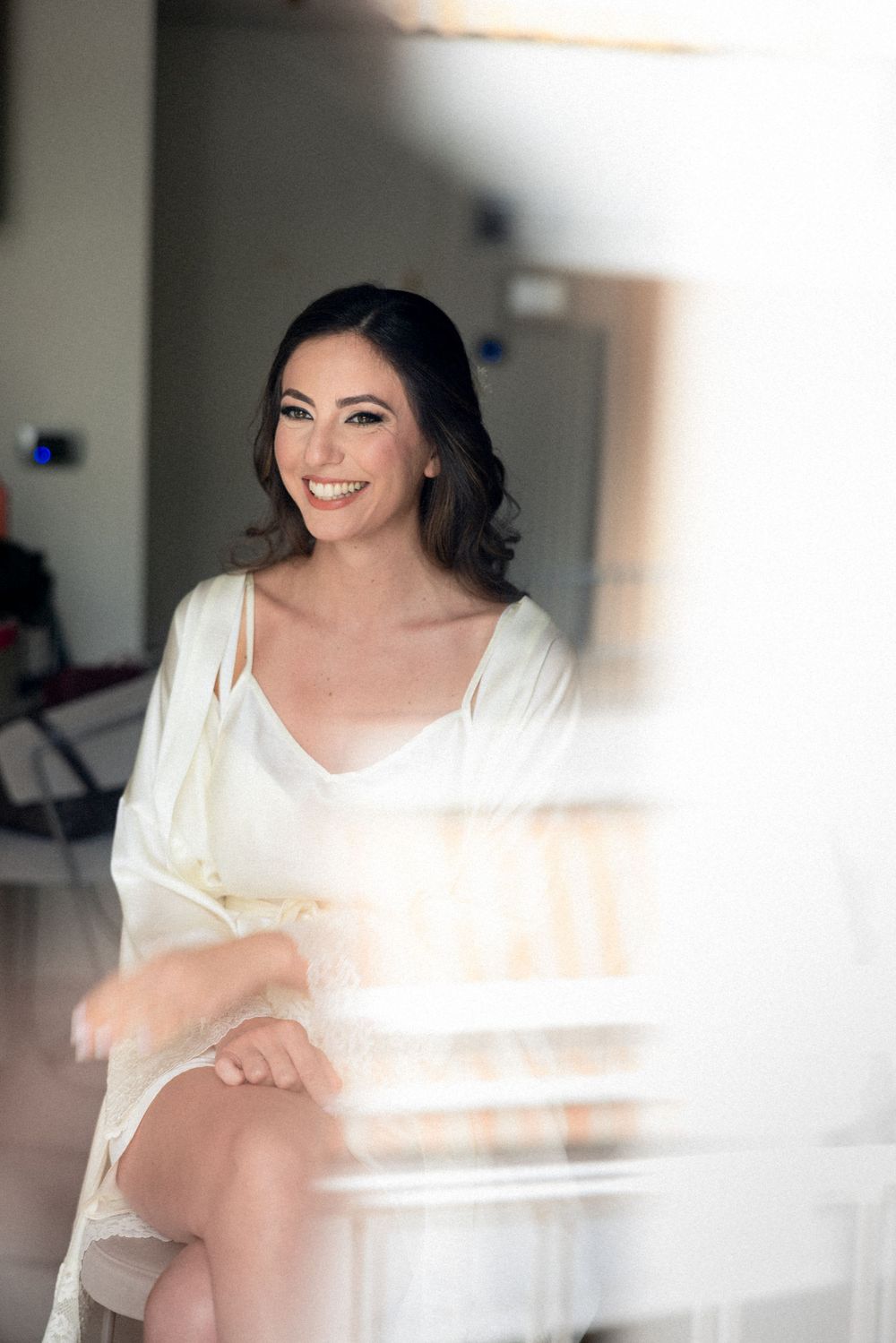 A person in a white dress sits indoors with soft, dreamy lighting creating an ethereal bridal portrait effect.