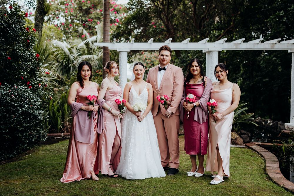 Wedding party in shades of pink and white poses together on a lush garden lawn.