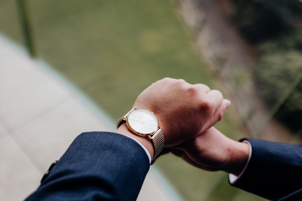 Groom in navy suit adjusts watch while getting ready for wedding ceremony.