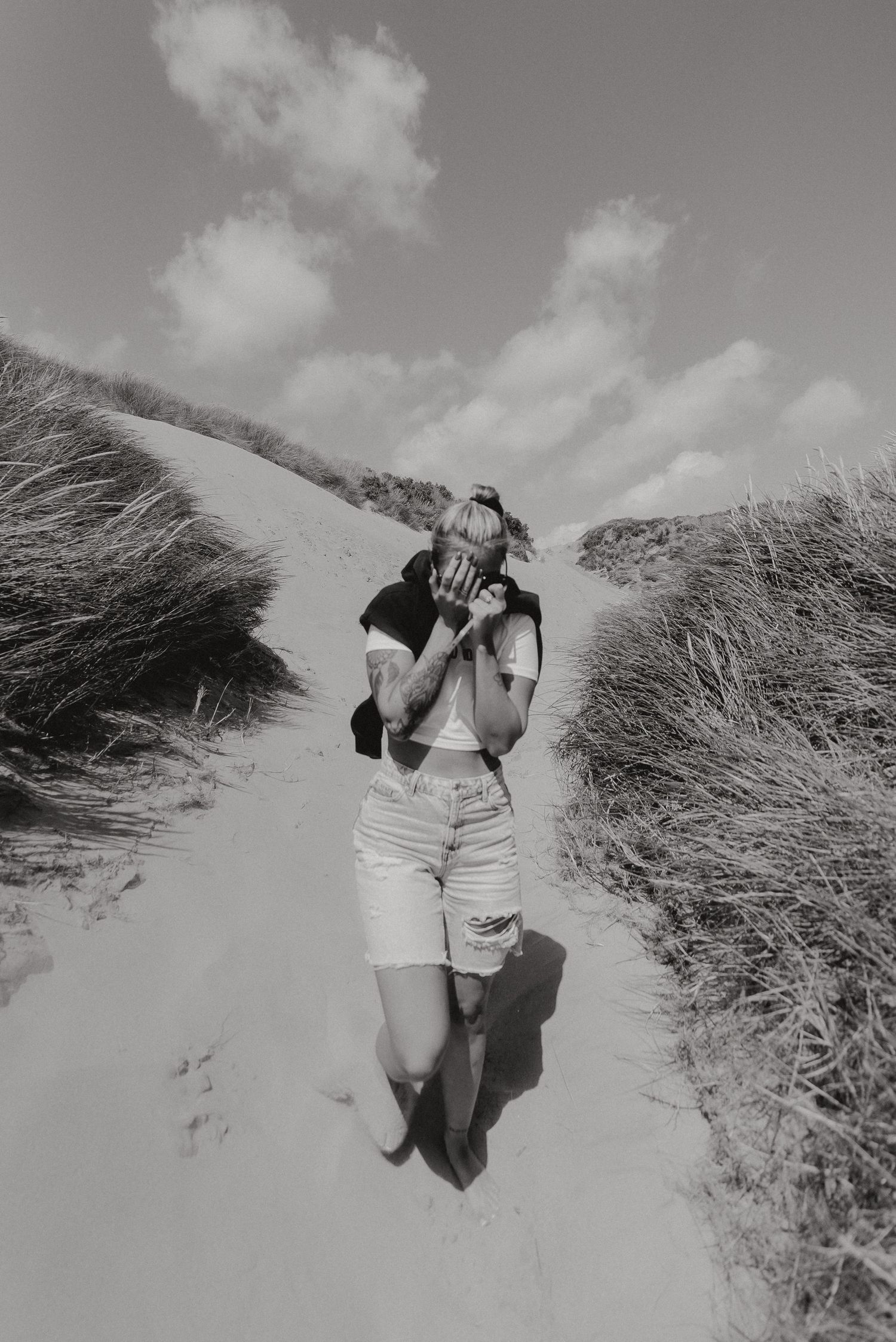 Black and white photo of person walking on sandy path through tall grass.