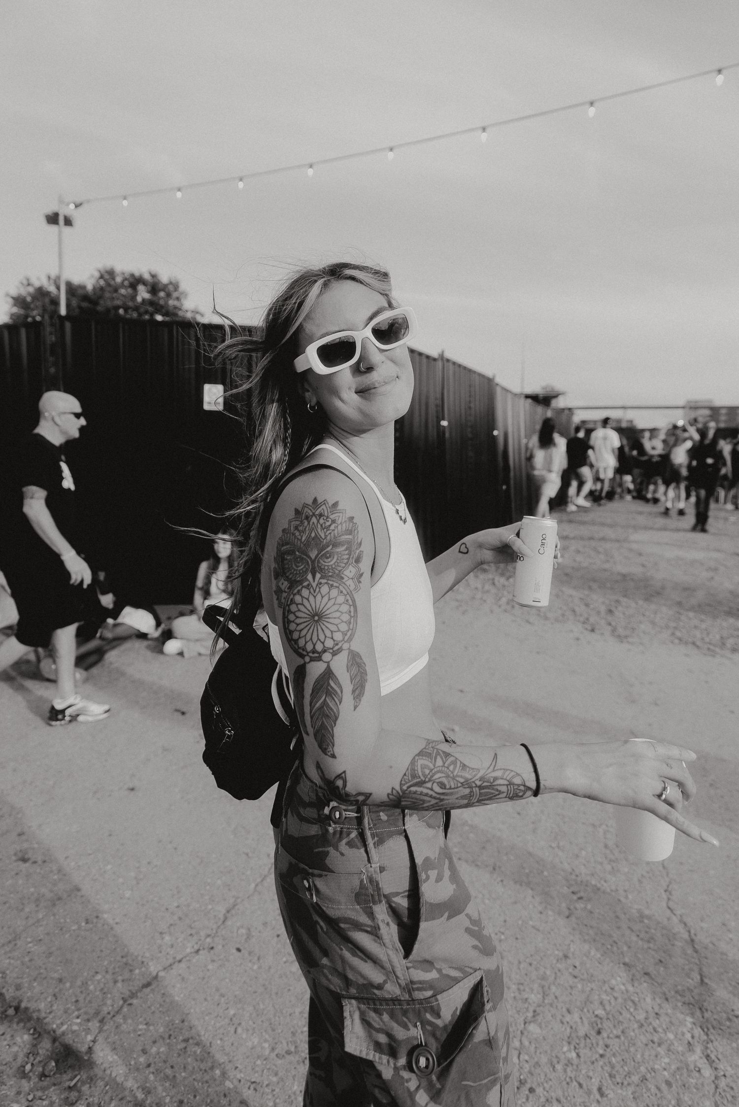 Black and white festival scene with someone showing off tattoos and sunglasses.