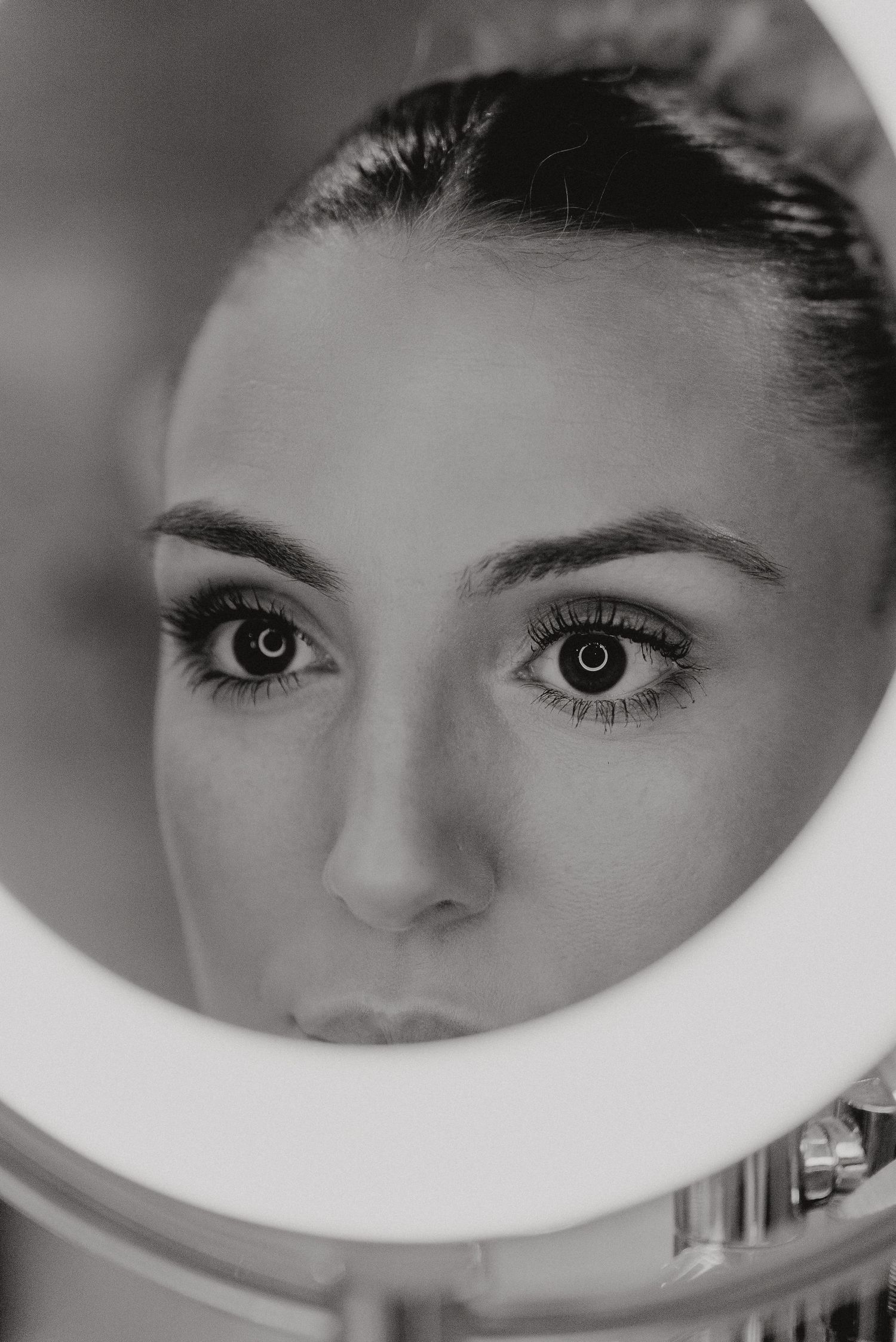 Black and white close-up reflection in circular mirror showing eyes and face with dramatic lighting.