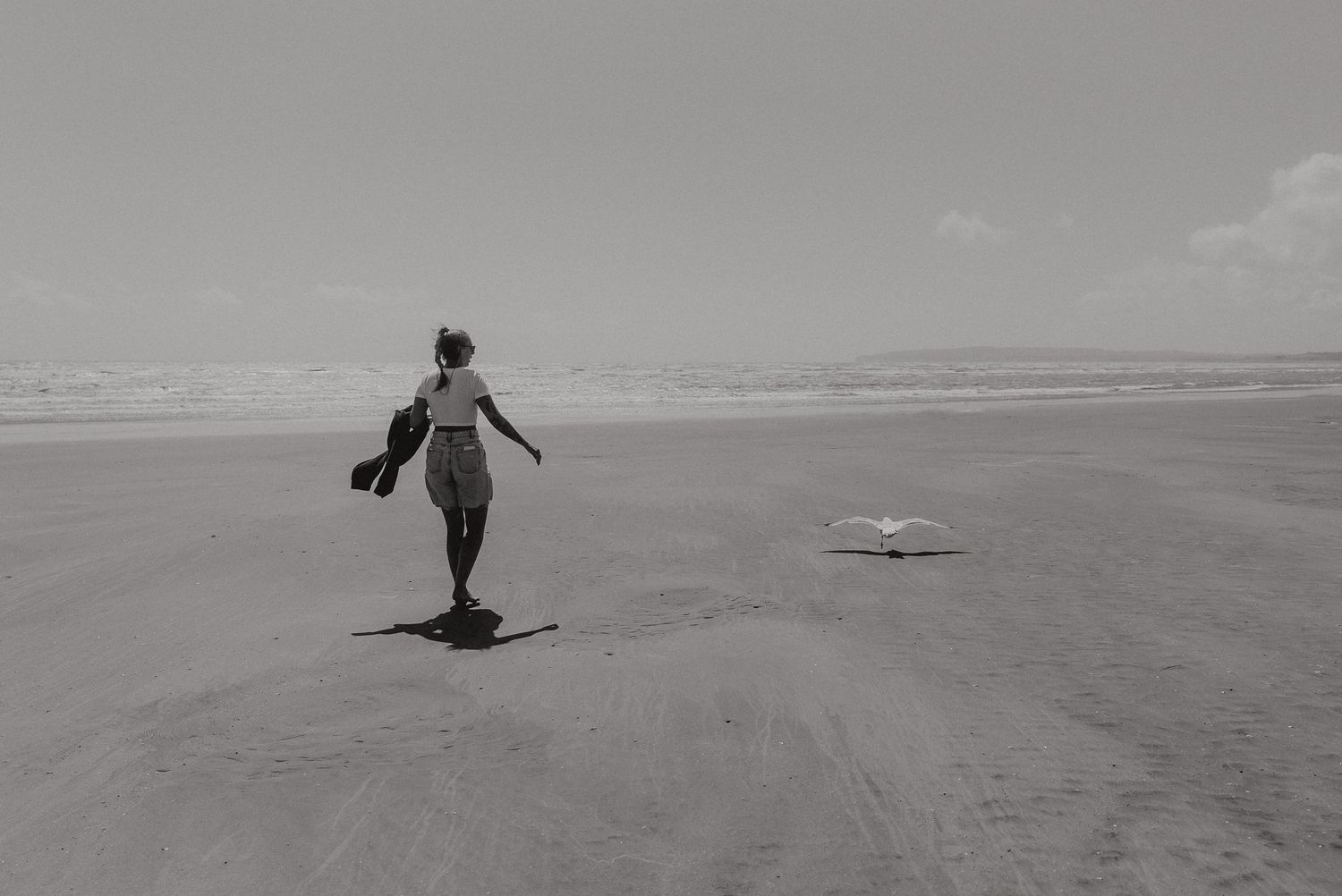 A silhouetted figure runs freely across an empty beach in black and white.