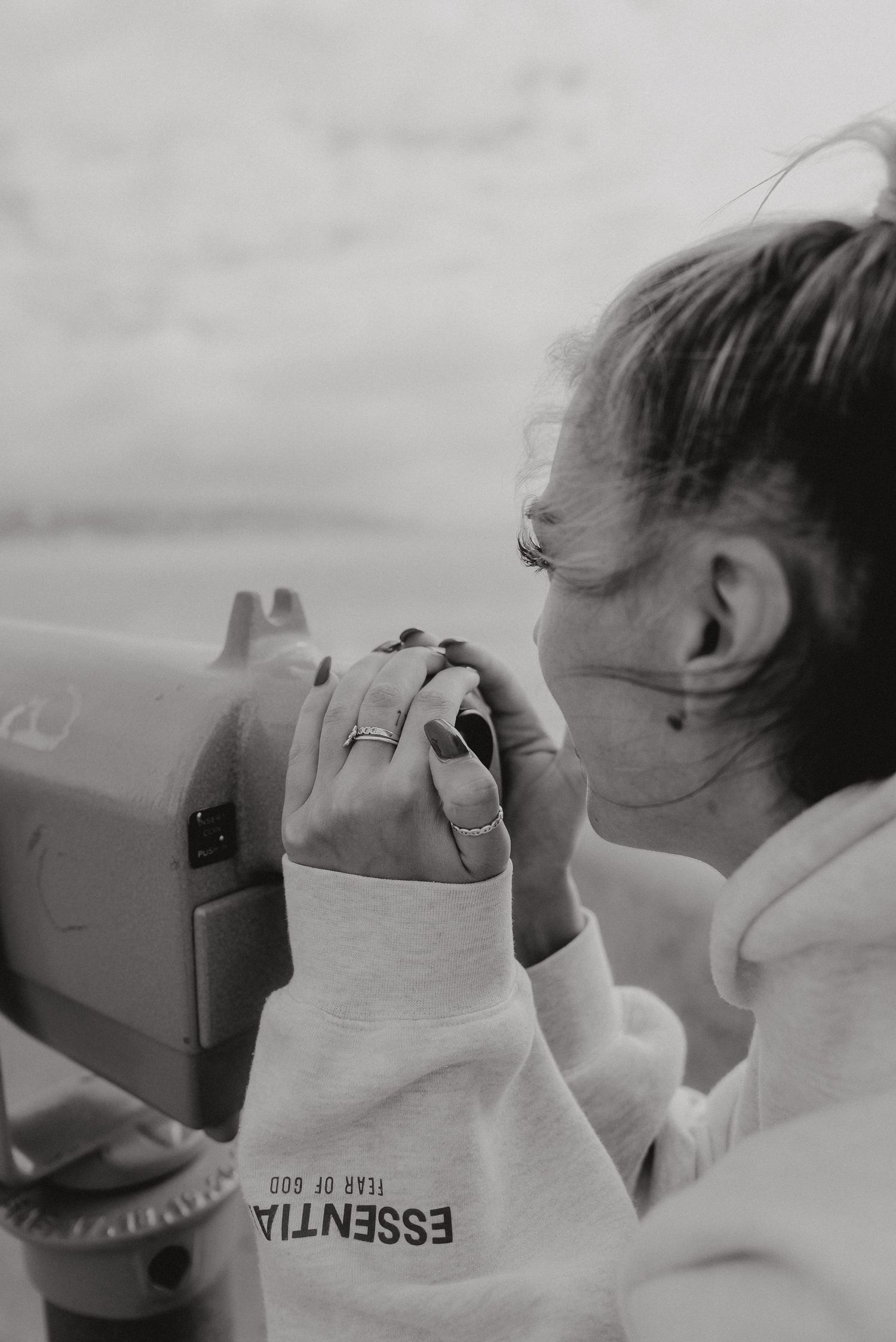 Person in white sweatshirt looking through viewfinder of camera against cloudy sky.