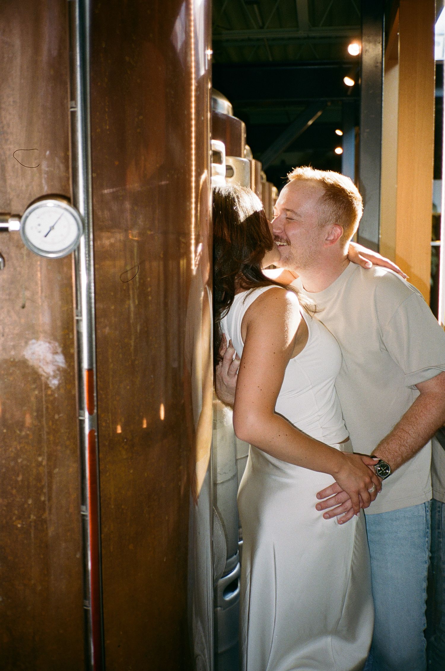 A romantic series of four photos showing a couple embracing and kissing in an industrial setting with copper columns.