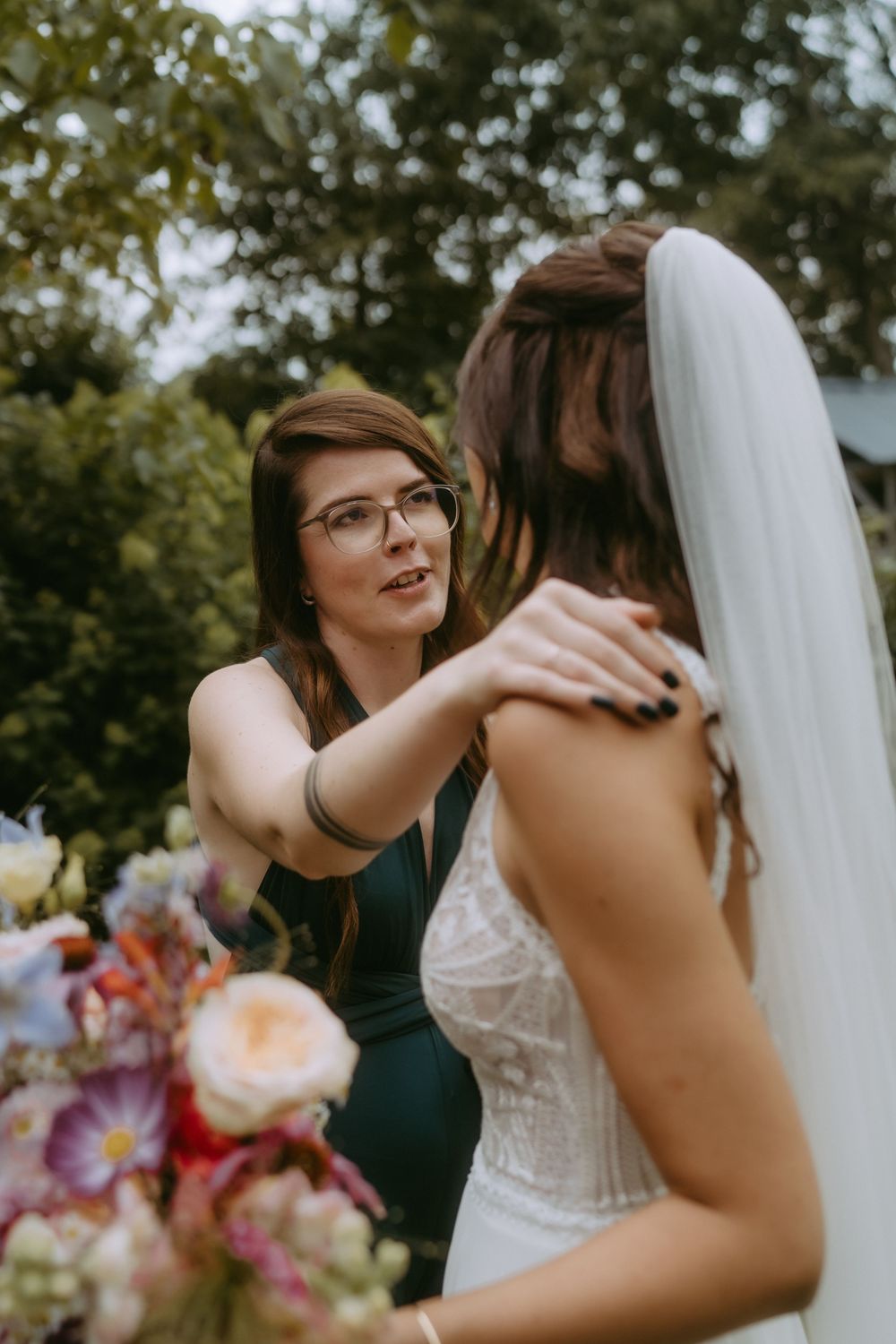 Emotional embrace between wedding party members outdoors with floral decorations.