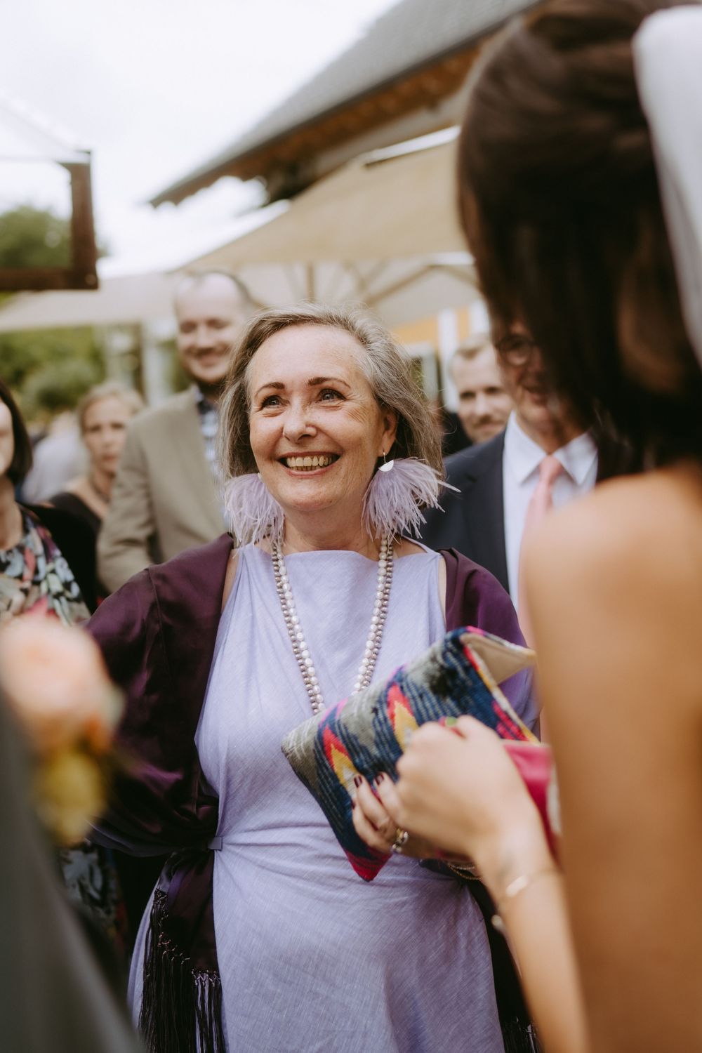 Guest wearing a lavender dress smiling joyfully at an outdoor wedding reception.