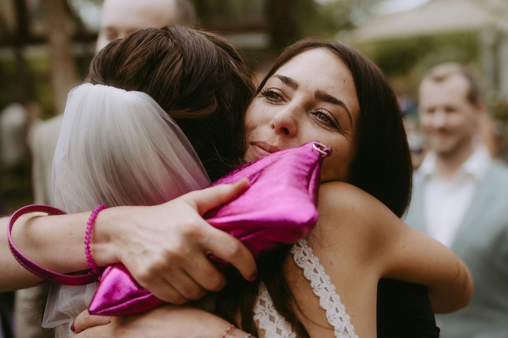 Wedding guests playfully blowing pink confetti during outdoor festivities.
