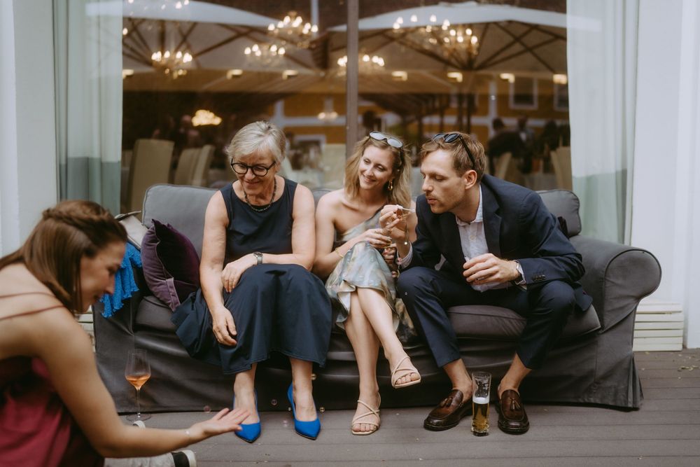 Wedding party lounges casually on gray couch during pre-ceremony preparations.