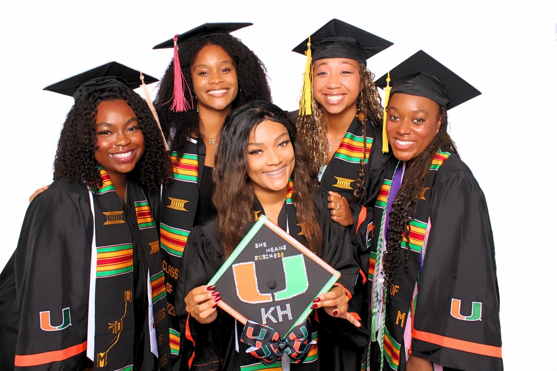 A group of graduates in black caps and gowns with colorful kente stoles celebrate during commencement ceremony.