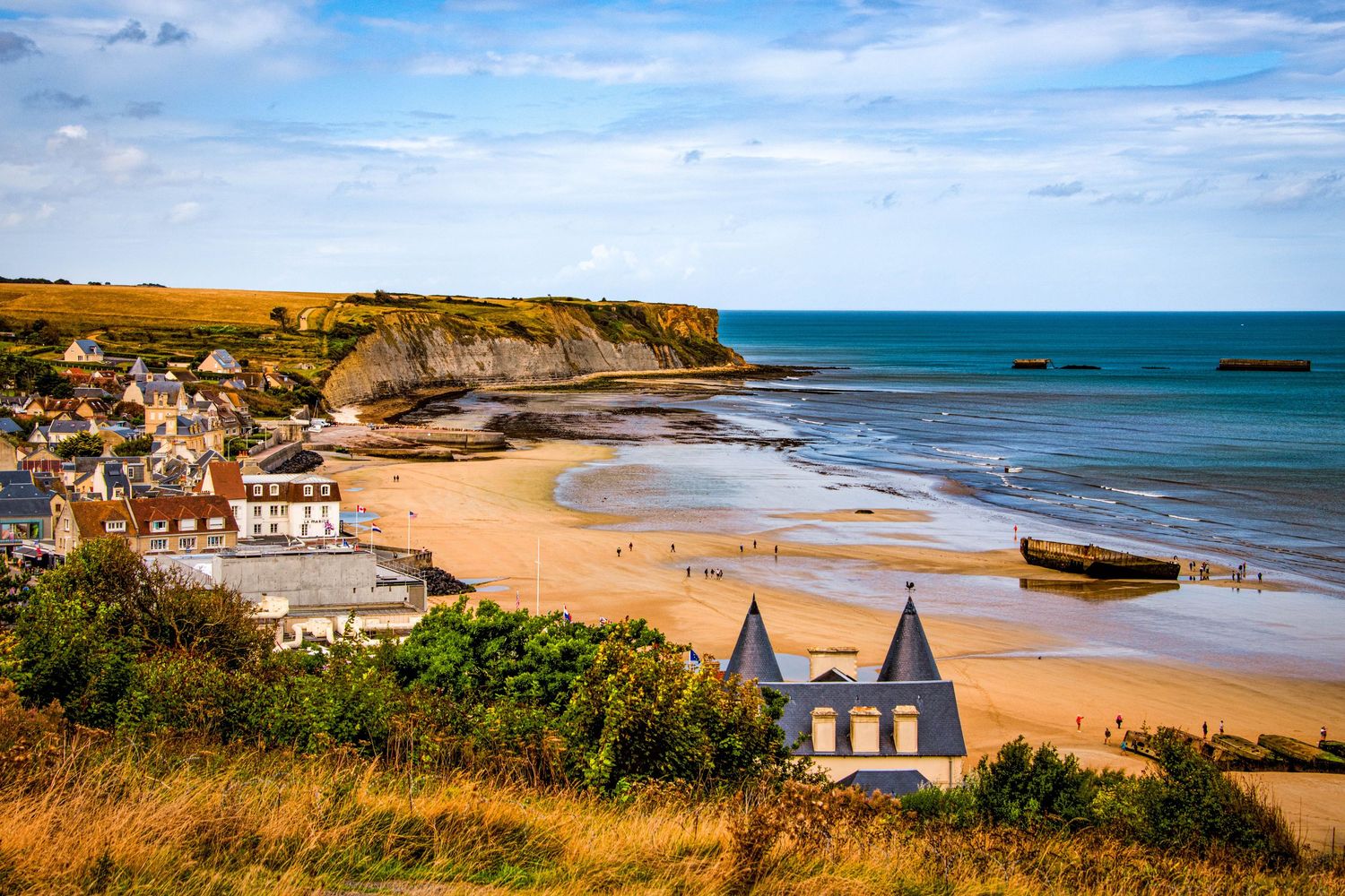 Panoramic view of a scenic coastal town with sandy beaches and rugged cliffs along the turquoise ocean shoreline.
