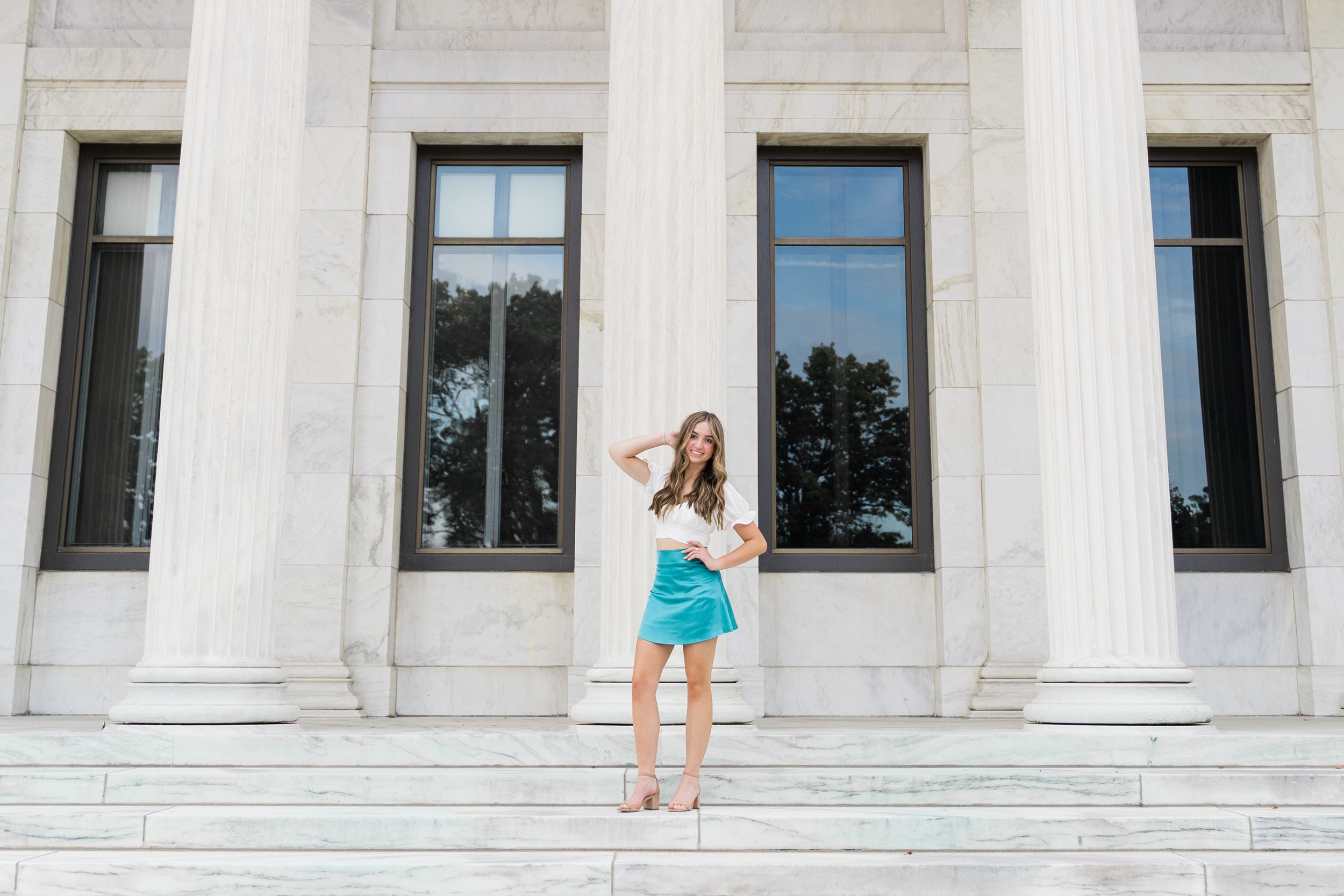 A row of people in colorful summer outfits pose on the steps of a white marble building with columns.