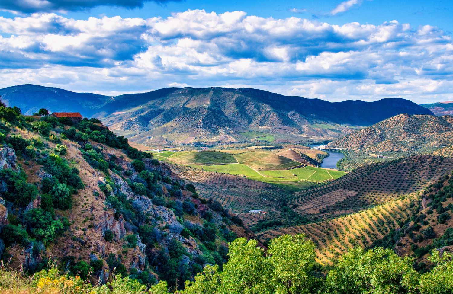 Panoramic mountain landscape with rolling hills, lush valleys, and dramatic cloudy skies stretching across the horizon.