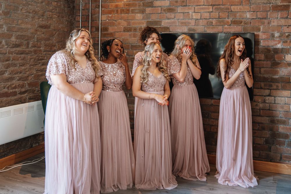 Five bridesmaids in dusty pink sequin and tulle gowns reacting with surprise and joy before the wedding.