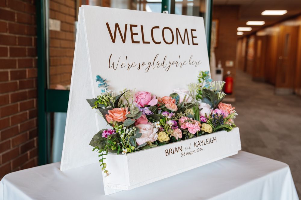 Wedding welcome sign for Brian and Kayleigh decorated with colorful fresh flowers on a white easel.