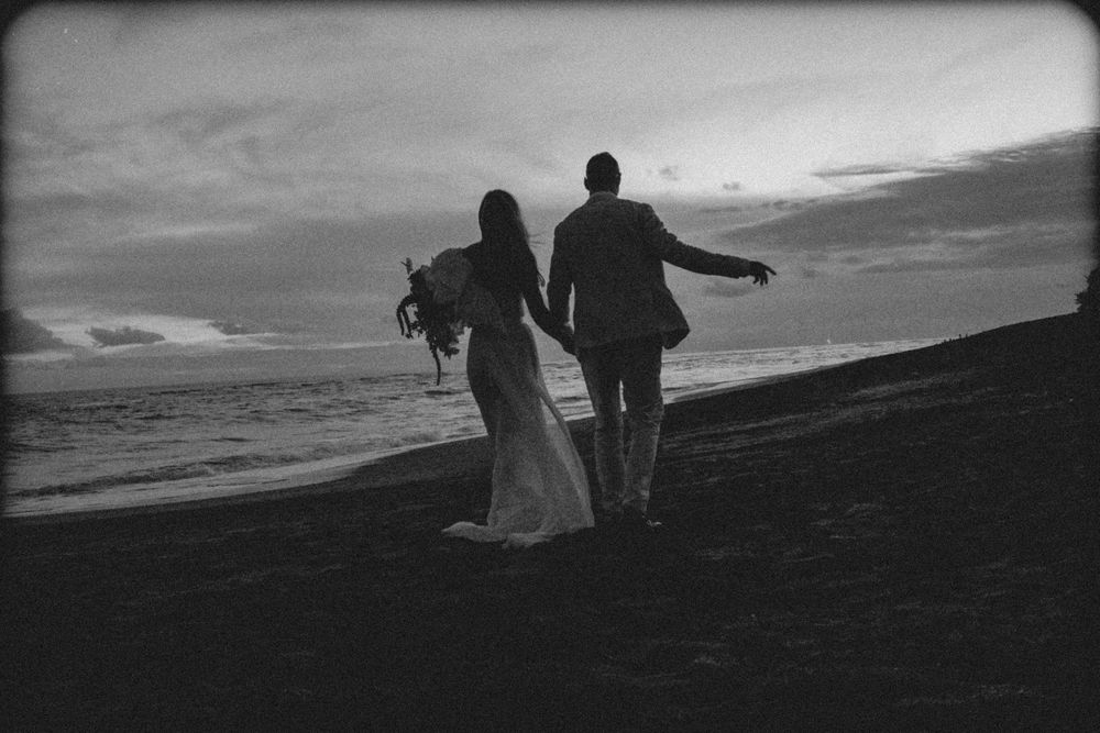 Silhouetted figures stand atop a hillside against a dramatic cloudy sky at sunset.
