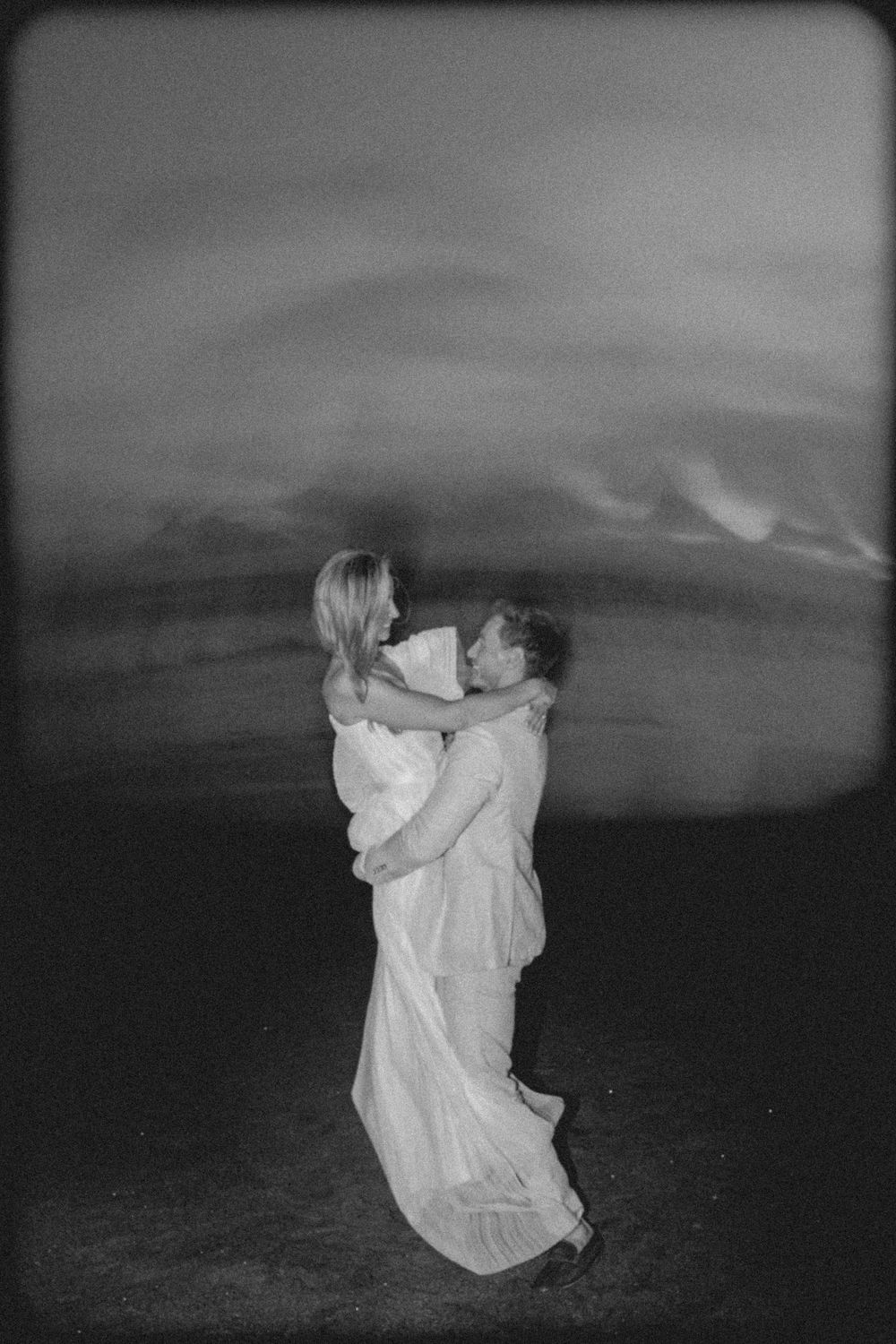 A sequence of black and white photographs showing figures in white flowing fabric dancing against a moody landscape.