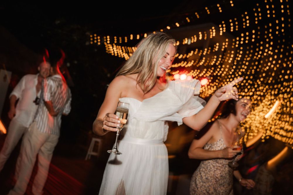 Wedding guests dance under twinkling string lights during an evening reception celebration.