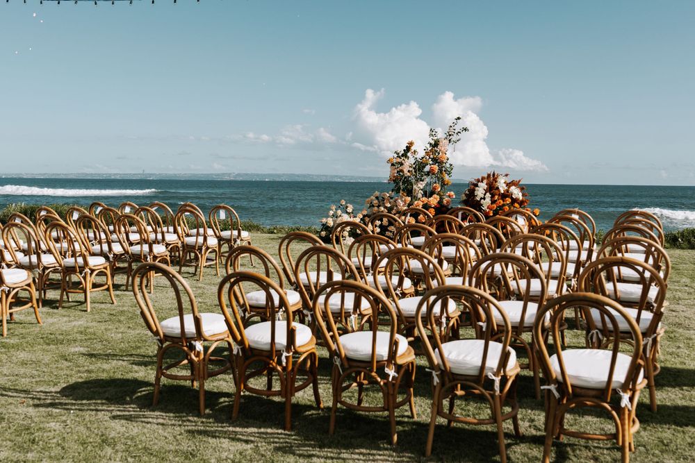 Empty wooden chairs arranged in rows on a beach for an outdoor wedding ceremony with ocean views at sunset.