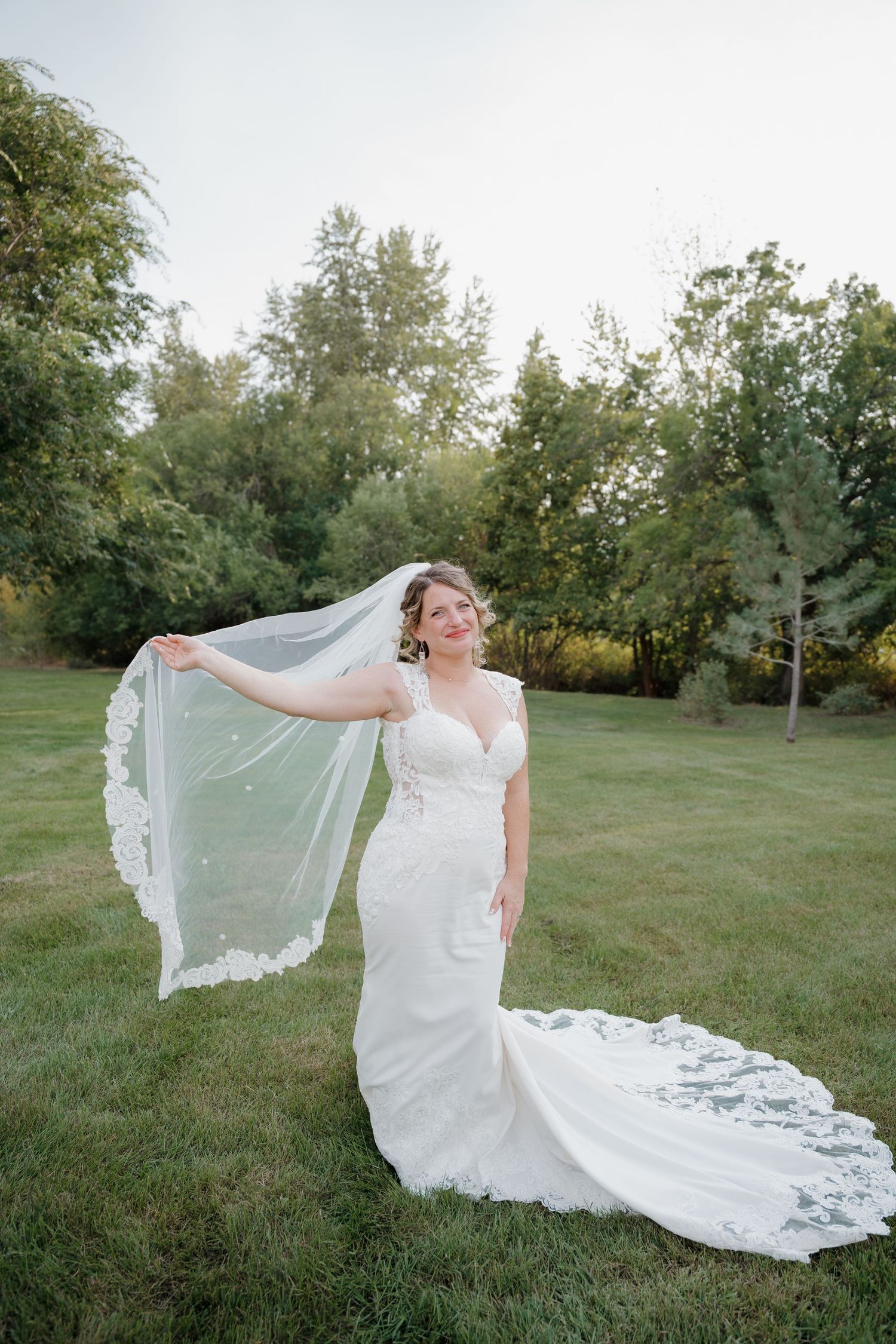 A flowing white wedding dress with lace details and long train captured in a series of romantic outdoor photos on a grassy lawn.