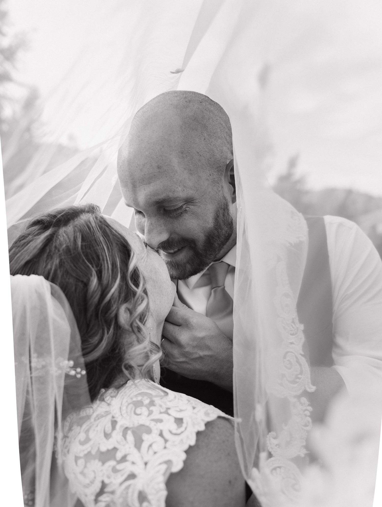 A tender black and white wedding portrait showing an intimate moment between newlyweds through a delicate veil.