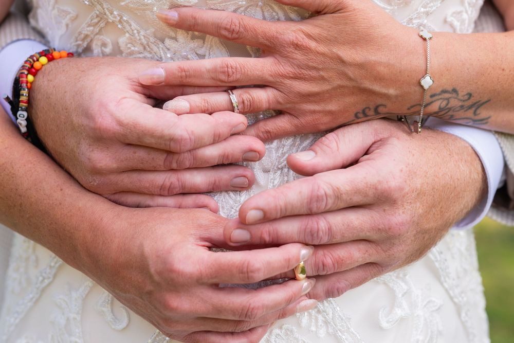 Multiple hands with rings and bracelets intertwined together against a light colored fabric background.