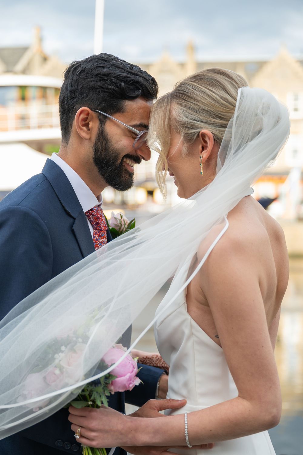 Romantic wedding couple sharing an intimate moment outdoors with flowing white veil.